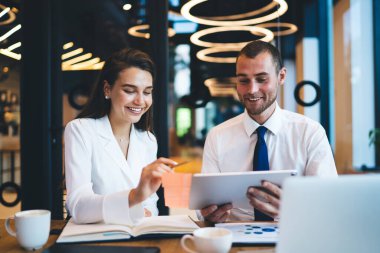 İyi giyimli, gülümseyen yüzlü meslektaşlar çalışma projesini tartışıyor, tablet kullanıyor ve iyi aydınlatılmış ofis alanında oturuyor.