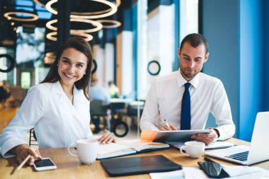 Modern ofiste gazete ve tabletle çalışan, notlar ve kahve fincanlarıyla ahşap masada oturan başarılı iyimser meslektaşlar.