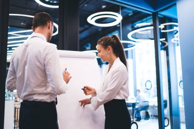 Yaratıcı genç ve pozitif iş arkadaşları resmi kıyafetler içinde boş tahtaya yakın duruyorlar ve ofiste projenin detaylarını tartışıyorlar.