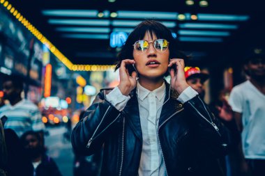 Elektronik gözlüklü modaya uygun kadın portresi. Ses kitabı dinlemek ve şehir merkezinde yürümek için kameraya bakıyor. Kulaklıkla Z jenerasyonu.