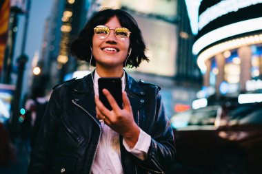 Modern cep telefonu teknolojisine sahip neşeli bir blog yazarı. Şehir sokağında web sohbeti yapıyor. Elektronik kulaklıklarıyla mutlu bir Z nesli.