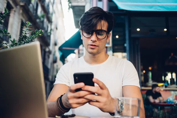 外で仕事をしながらスマートフォンやテキストメッセージを使ってバルセロナのカフェに座っている眼鏡やブレスレットに集中カリスマ的な男 — ストック写真