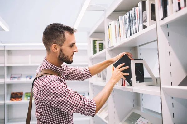 现代书店中穿着休闲装 站在书架上看书的严肃年轻男性侧观 — 图库照片