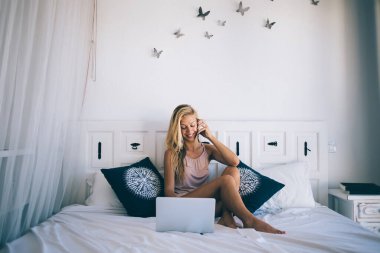 Kafkasyalı mutlu bir kadın rahat bir evde rahat bir yatakta dinleniyor ve en iyi arkadaşıyla akıllı telefon görüşmeleri sırasında gülümsüyor. Laptop ağı kurarken sosyal yayını tartışıyorlar.