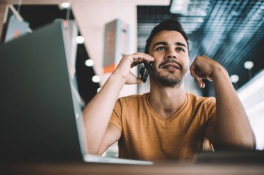 Kendine güvenen serbest çalışan, günlük kıyafetler giyen, akıllı telefon kullanan, iş yerindeki masada oturma stratejisini tartışan bir iş arkadaşı.