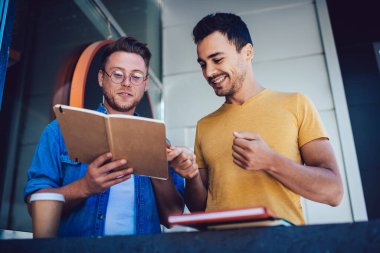 İçerik öğrencilerinin günlük kıyafetleri ve gözlükleriyle ellerinde not defteriyle iş yerindeki notları işaret eden adama ödevlerini açıklarken.