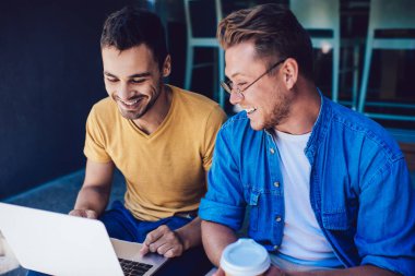 Neşeli milenyum çocuğu, tek kullanımlık kahvesi ve erkek arkadaşı laptopta video izlerken eğleniyor ve gülüyor.