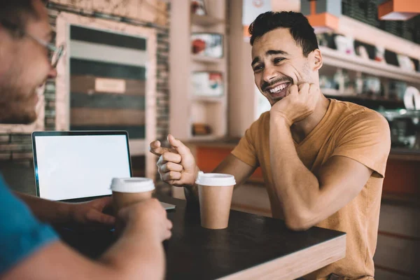 Happy cheerful caucasian man laughing during conversation with friend in coffee shop. colleagues students talking to each other enjoying prosperous startup project using technology with blank scree