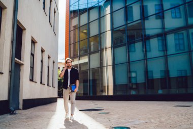 Şık sakallı, gözlüklü, modaya uygun giysiler giyen, gündüzleri elinde defterlerle şehir merkezinde yürürken cep telefonuyla sohbet eden bir erkek.