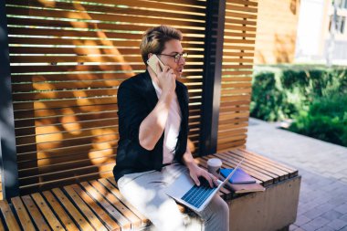 Kağıtlarla süslü şık kıyafetler içinde sakin bir serbest yazar. Kahverengi ahşap bankta otururken ve netbook ile sokakta iletişim kurarken gözlerini kaçırıp telefon görüşmesi yapıyor.