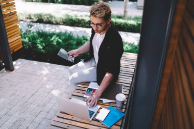 Yazın bankta otururken bilgisayardaki e-postaları kontrol eden ve gazetelerle çalışan şık bir erkeğin yukarıdan görünüşü
