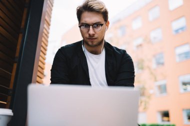 Siyah ceketli, beyaz tişörtlü, netbook 'lu, sokak kentinde ahşap bankta oturan genç ve zeki bir erkekten.