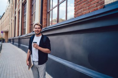 Sırt çantalı ve not defterli rahat gülümseyen genç adam. Sokakta rahatlayıp başka yere bakıyor.