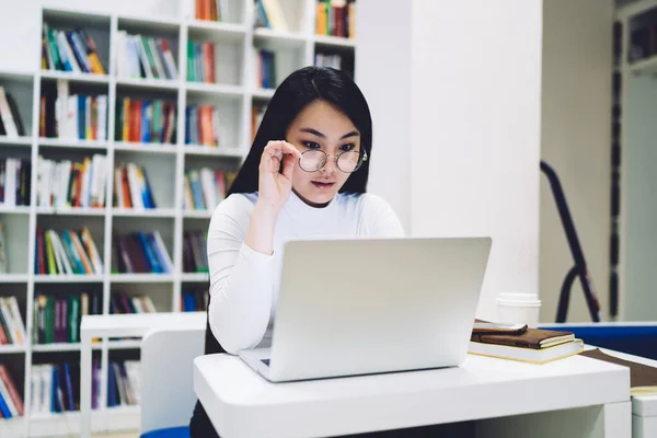 아시아 벌리고 안경을 책상에 화면에 집중하고 도서관에서 노트북으로 작용하는 — 스톡 사진