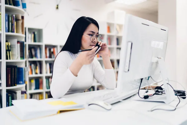 옷차림의 아시아 매니저가 책상에 앉아서 컴퓨터 화면을 진지하게 일하는 전화로 — 스톡 사진