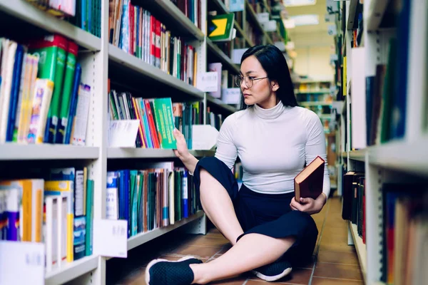 Σοβαρή Νεαρή Ασιάτισσα Φοιτήτρια Κάθεται Στο Πάτωμα Δίπλα Στη Βιβλιοθήκη — Φωτογραφία Αρχείου