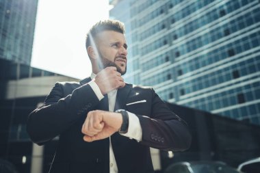 Sabırsız, stresli, takım elbiseli iş adamının düşük açısı. Dev modern iş merkezinin önünde duruyor.