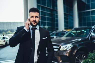 Siyah kravatlı, kendine güvenen sakallı adam modern şehrin sokaklarında iş arkadaşı ile sohbet etmek için akıllı telefon kullanıyor.