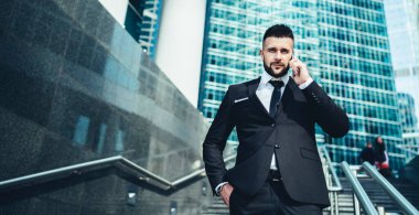 Yetişkin klas bir adam cep telefonuyla konuşuyor. El ele tutuşup binaların arasındaki merdivenlerde kameraya bakıyor.