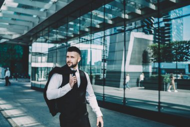 Yakışıklı, rahat, şık giyinen, ceketli, omuzları üzerinde gezen, camlara bakan ve şehir merkezindeki modern binaların yansımasını yansıtan bir yönetici.