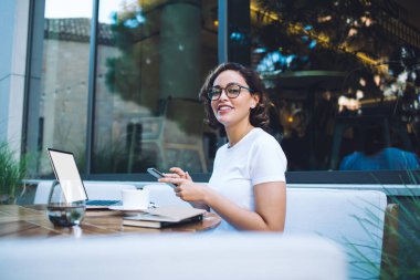 Bilgisayarda çalışırken ve modern kafede çay içerken akıllı telefondaki mutlu kadın mesajlarından.
