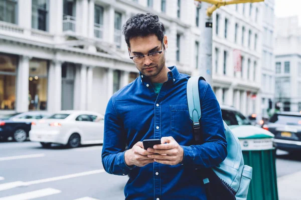 白天站在繁忙的城市街道上 以身穿蓝色衬衫 戴着眼镜 头戴智能手机背包的英俊成年男子为焦点 — 图库照片
