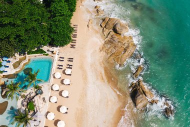 Açık havuzu ve güneş pansiyonları olan ilk hat plaj otelinin havadan görünüşü. Yaz tatillerinin kuş bakışı manzarası, turkuaz deniz suyu ve temiz kum kıyısındaki şemsiyeler.