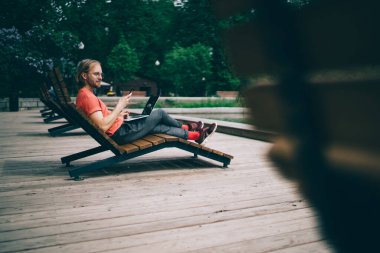 Uzaktan kumandalı parkta dinlenirken, günlük kıyafetli bir adamın dinlenme odasında oturması ve sosyal medyaya akıllı telefondan bakması.