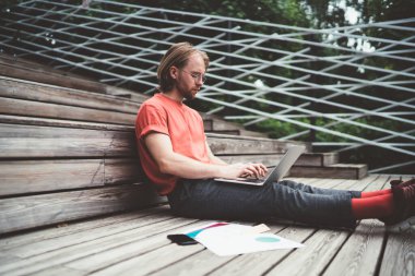 Sokakta merdivenlerde otururken dizüstü bilgisayarda çalışan odaklanmış adamın yan görüntüsü.