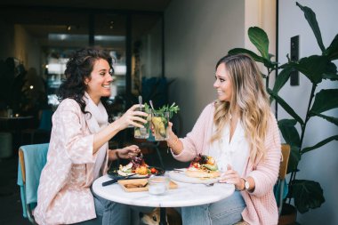 Modayı takip eden Kafkasyalı mutlu bayan arkadaşlar yemek molasında gülümseyip bardakla soğuk kokteyller içerler. Pozitif kadın meslektaşlar, boş zamanlarında buluşmaktan ve sohbet etmekten memnun olurlar.