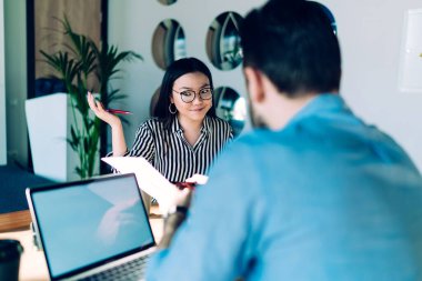 Bilgisayarın başında boş ekranla oturan ve gazetelere bakan Asyalı genç bir kadınla konuşan adamın arka planı.