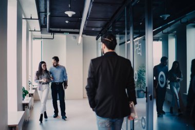 İş adamlarının iş arkadaşlarıyla buluşmaya giderken, genç ve ciddi bir çiftin iş yerinde erkeklerin önünde yürüdüğü arka plan.