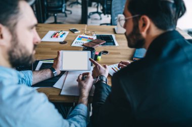 Akıllı, başarılı, düşünceli, özgüvenli yöneticiler ofis masasında çalışırken başlangıç projesini tablet üzerinde beyaz ekranla analiz etmek için işbirliği yapıyorlar.