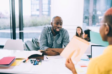 Hüsrana uğramış Afrikalı Amerikalı erkek, ürün satan kadın işadamının önünde masada otururken belgede kötü satış sonuçlarını veya hataları açıklıyor. 