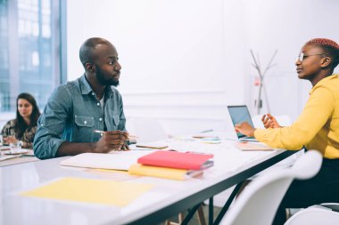 Siyahi yaratıcı ciddi çalışanlar, iş yerindeki belgeler ve dizüstü bilgisayarlarla işbirliği sırasında birbirlerine bakarak başlangıç projesini tartışıyor ve düşüncelerini yazıyorlar.