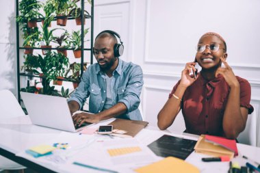 Afro-Amerikalı, gülümseyen bir kadın, iş yerinden telefonla arıyor. Kulaklıklı bir zenciyle konuşuyor. Kafede dizüstü bilgisayar kullanıyor.