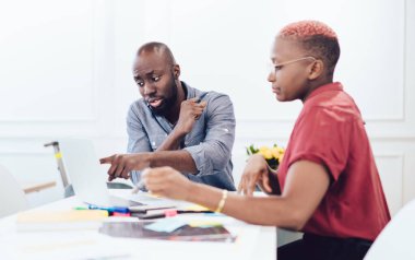Afro-Amerikan ciddi modern çalışanlar dizüstü bilgisayarla çalışıyor ve çalışma fikirlerini tartışıyorlar ofiste keçeli kalemlerle masada oturuyorlar