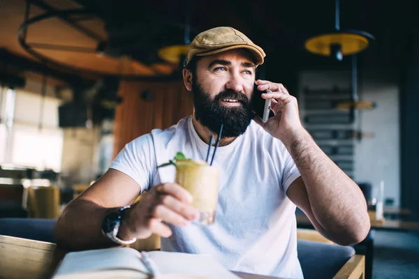 Positive Bearded Man Talking Smartphone Looking Away While Drinking Cold — Stock Photo, Image