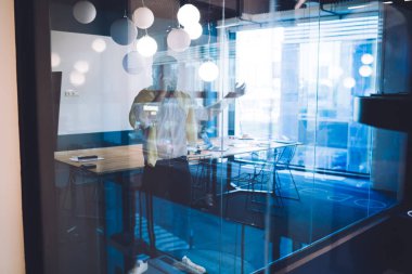 Modern konferans odasında masanın yanında duran ve akıllı telefondan iş arkadaşınla konuşan pozitif erkek girişimcinin cam görüşü sayesinde.