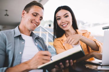 Neşeli, sıradan bir genç adam notlar yazarken şık bayan meslektaşım da deftere işaret ediyor ve açık kafedeki kameraya bakıyor.