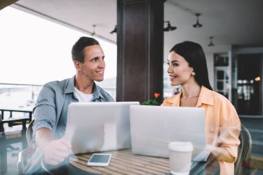 Lokanta terasında birlikte oturan neşeli arkadaşlar birbirlerine gülümsüyor ve kahve içerken dizüstü bilgisayarlarında araştırma yapıyorlar.