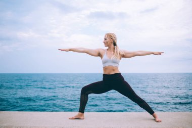 Siyah taytlı zayıf sarışın kadın ve beyaz bluzlu savaşçı yoga egzersizleri sırasında iki asana.