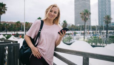 Modern cep telefonu aygıtını elinde tutan Kafkasyalı çekici kullanıcının yarım boy portresi, akıllı telefon aygıtında 4G 'ye bağlı turistik sırt çantalı güzel bir bayan gezgin.