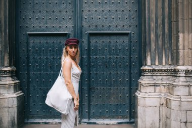 Mimarinin yanında tarihi kapıları olan şık bir çevre çantasıyla yarım boyda gezgin kadın portresi, bordo şapkalı moda giyinmiş hippi kız turistik kasabayı ziyaret ediyor.