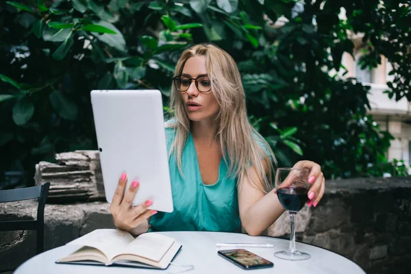 Millennial female user in classic eyewear watching web video during web networking on touch pad, beautiful journalist in spectacles doing information research on digital tablet connecting to 4g