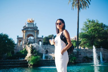 Moda giyinmiş beyaz kadın portresi ve güneş gözlüğü şehir ortamında dinleniyor. Çekici genç 20 'li yaşlarda kadın hipster kokteyl bardağı tutuyor. Yaz tatilinin tadını çıkarıyor.