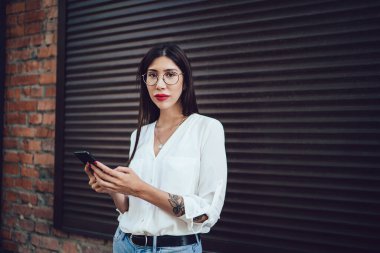 Modern cep telefonu cihazıyla kentsel ortamda poz veren kadın neslinin yarım boy portresi, cep telefonuyla internete bağlanmak için 4G kablosuz internet kullanan çekici kadın nüfuz blogcusu