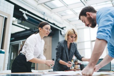 Kendine güvenen, kahverengi saçlı bir kadının yanında çalışan çekici bir kadın. Mavi gömlekli, kafası karışık, düşünceli, sakallı bir erkek arkadaşa bakıyor.
