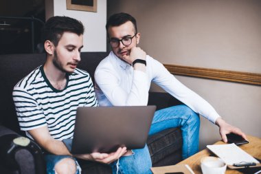 Düşünceli adamlar gündelik giysiler içinde tartışırken ve dizüstü bilgisayarda çalışırken masa masa oturup not tutuyorlardı.