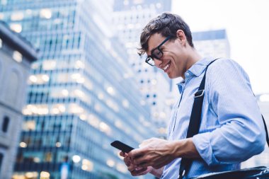 Tişörtlü ve gözlüklü bir adamın New York 'un yüksek binalarına gülümseyen bir şekilde mesajlaşması.